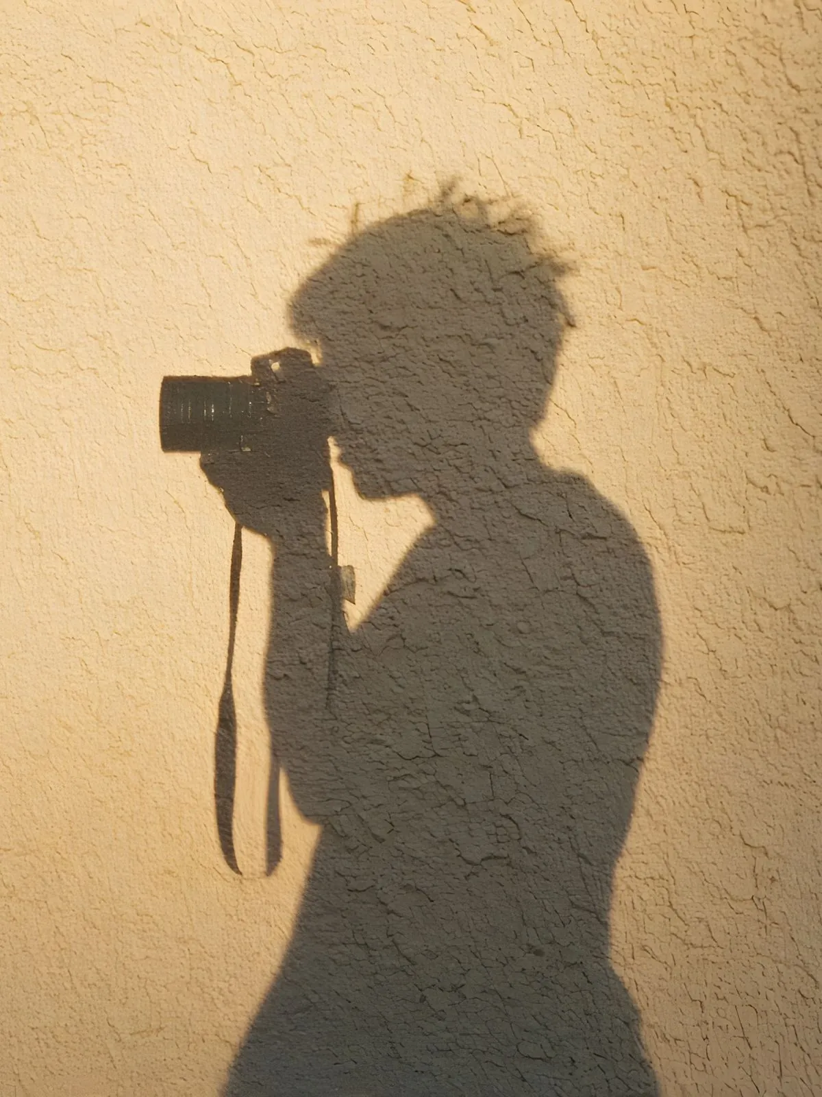 The shadow of Margot's hands and camera on a stucco wall